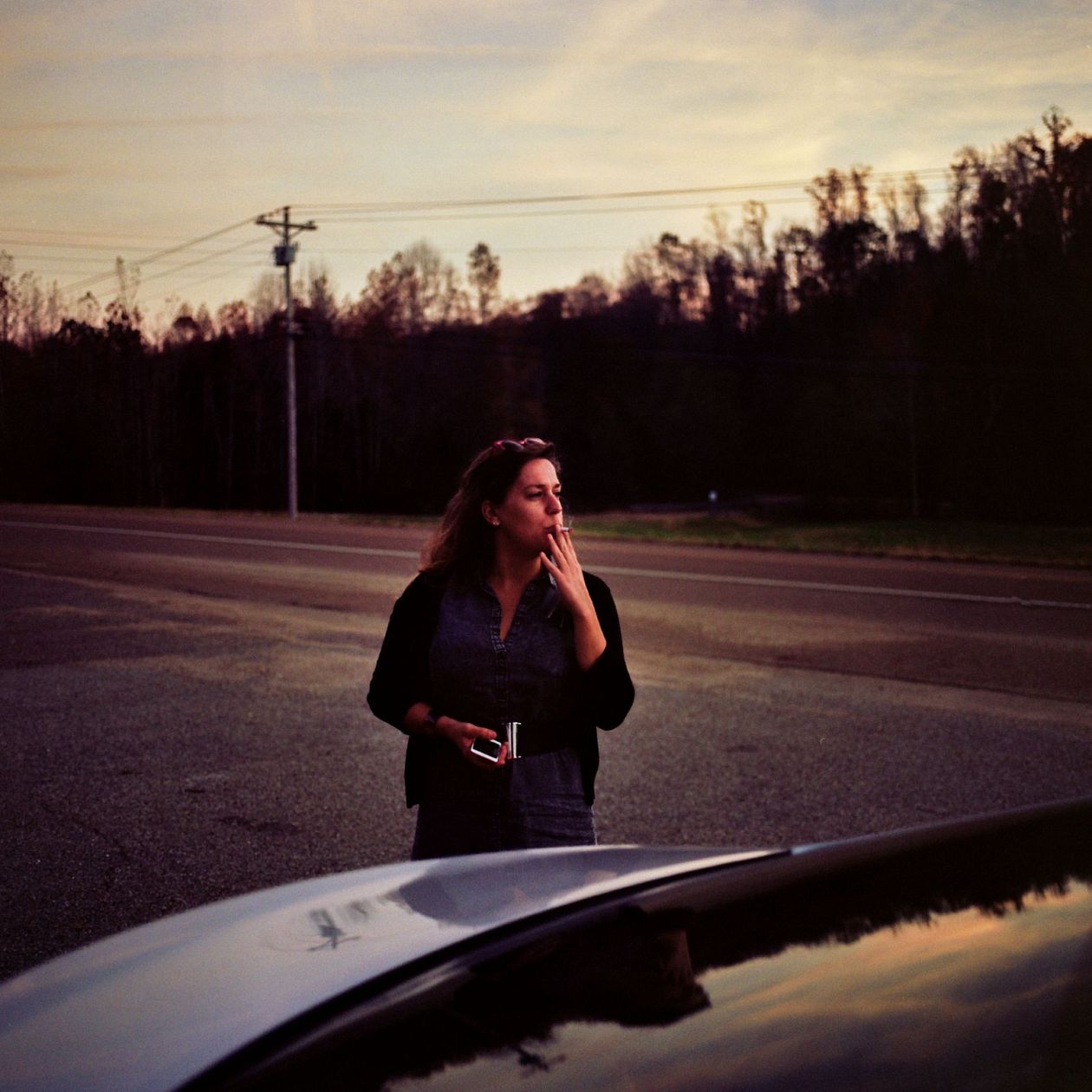 woman with mobile phone in the car on the road at sunset