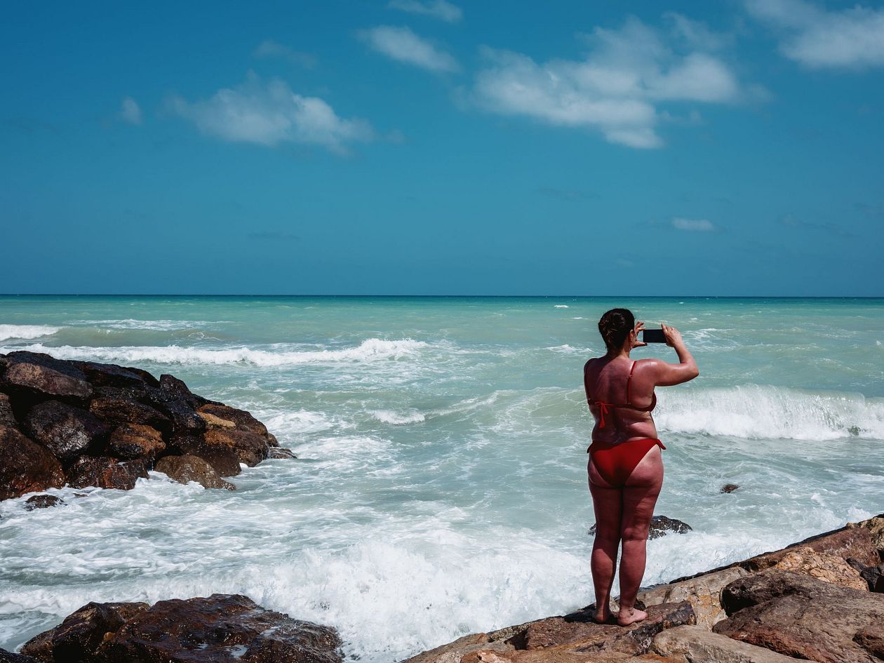 Young woman in red swimsuit standing on rock and looking at sea