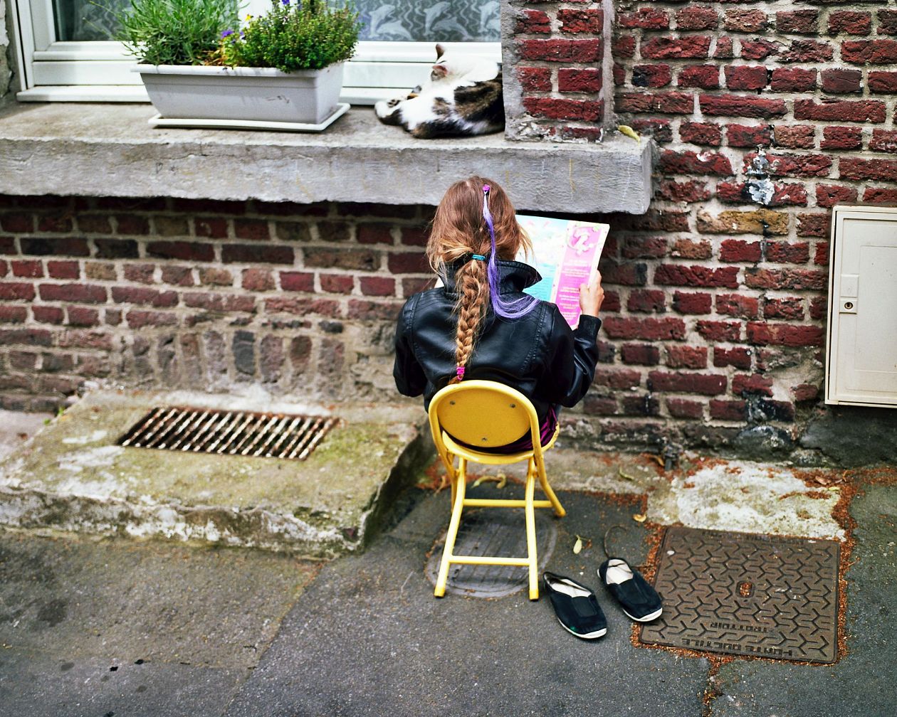 Little girl with long braids sitting on a chair in the street. Lille, France