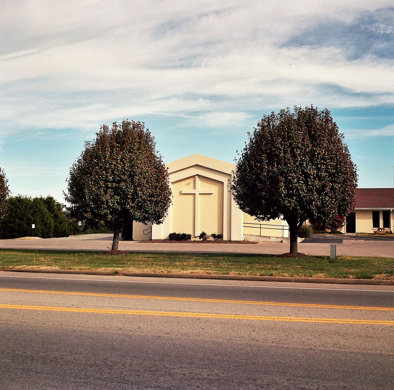 A small church on the side of a road with trees in the foreground.