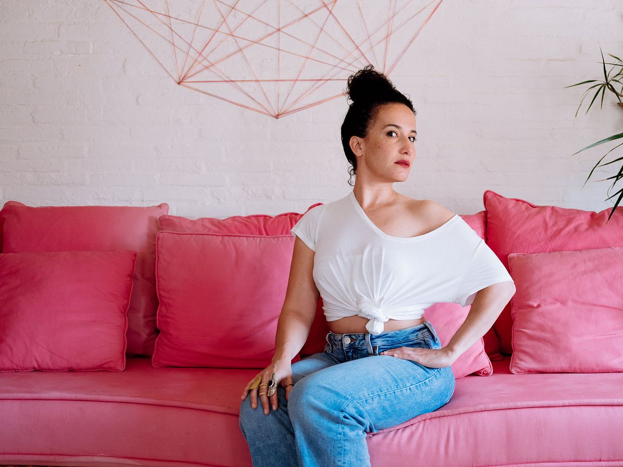woman in jeans and t-shirt sitting on pink sofa at home