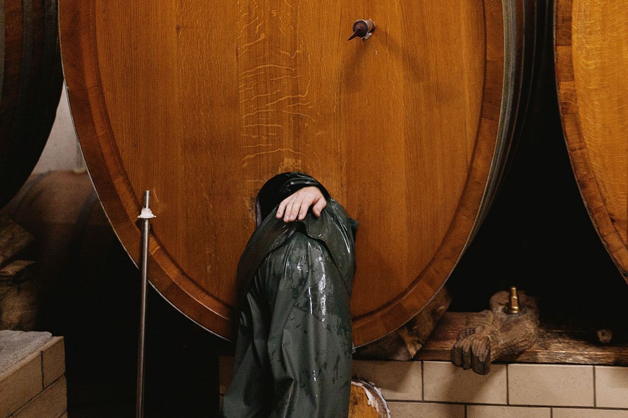 Wine cellar. A man in a green raincoat stands in front of a wooden barrel.